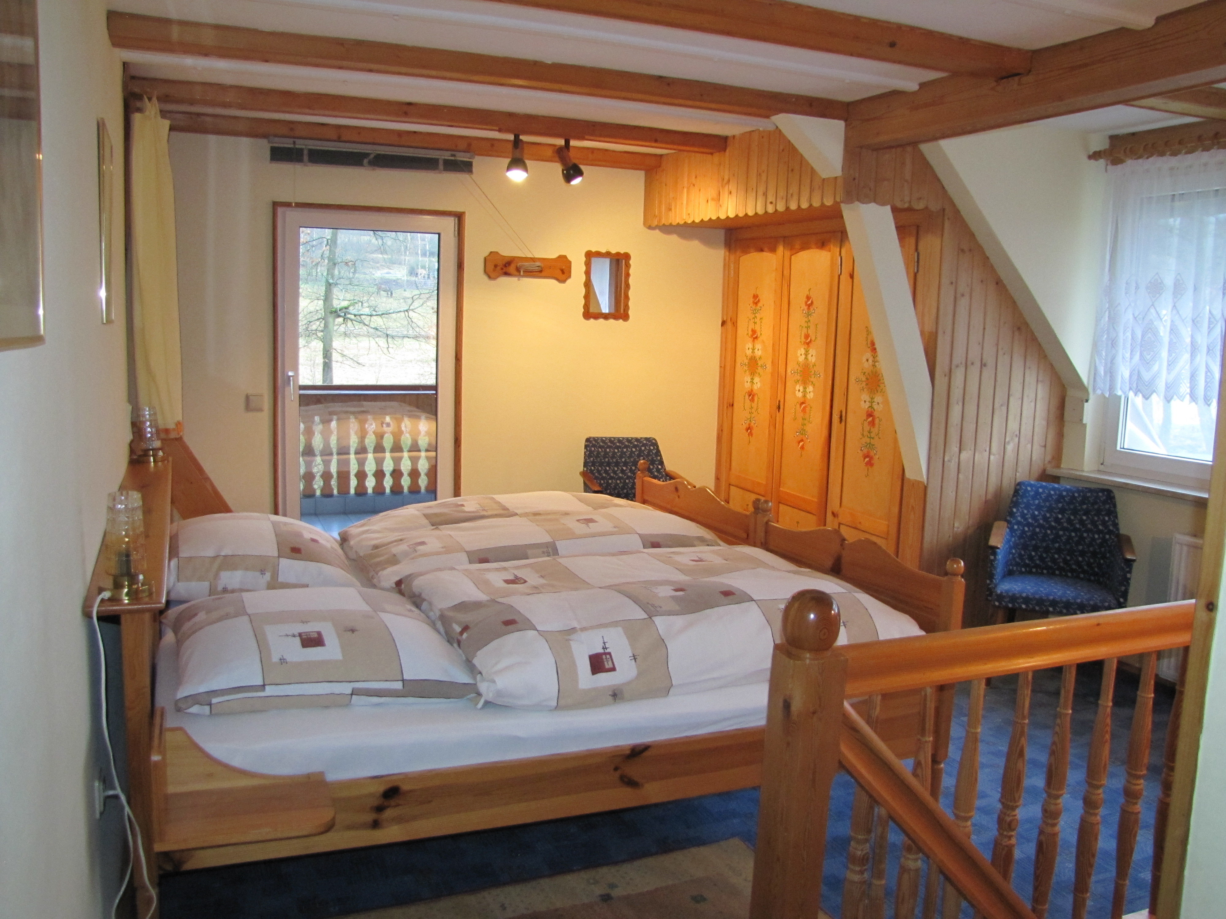 Schlafzimmer mit Holzdoppelbett, Kleiderschrank und Zugang zum Balkon